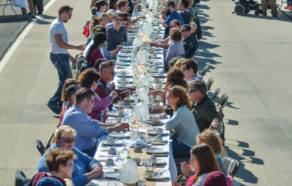 Dinner attendees line up on either side of a long table in the middle of the street, from the 500 Plates toolkit