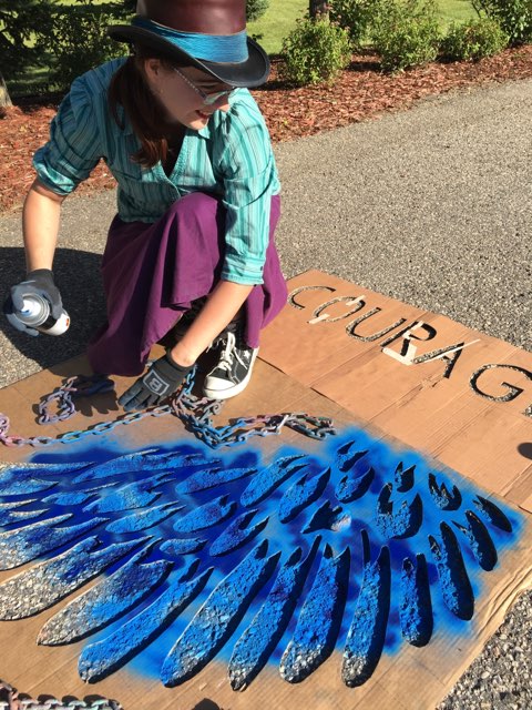 A person cutting a stencil with a blue wing and the word COURAGE