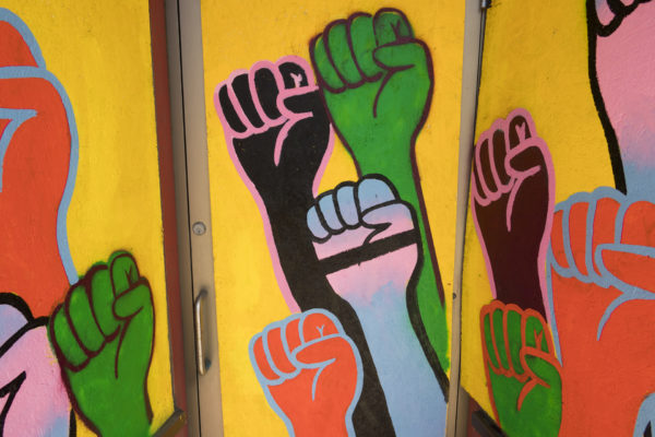 Mural of black, green, red and trans fists on a yellow background from Artists Respond: On Plywood