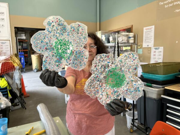An Artist holding up large, plastic flower shapes with white petals and colorful speckles, and a green center.